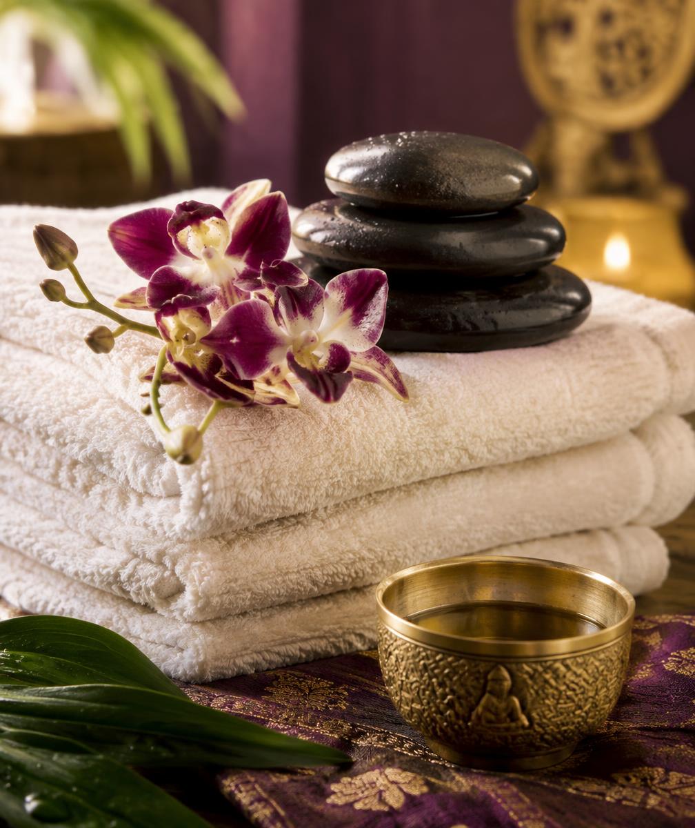 Folded towels with hot stones, an orchid and a brass bowl of oil